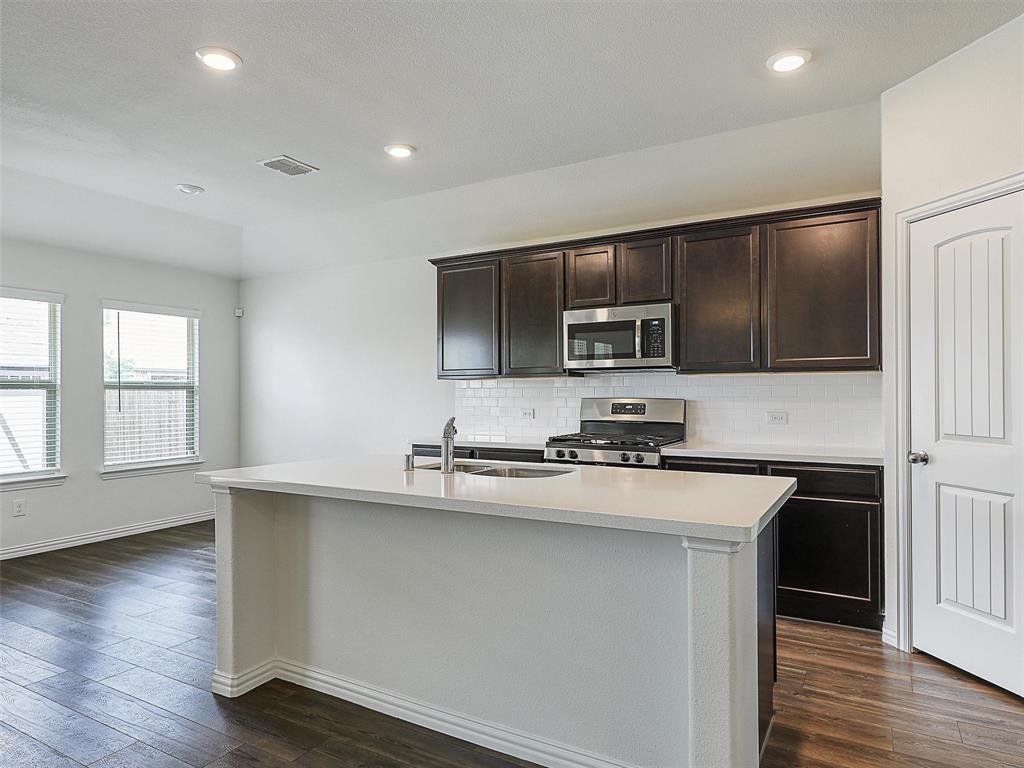 910 Torrey Avenue Princeton, TX 75407 - Photo 12 of 39 a kitchen with stainless steel appliances a sink dishwasher a stove top oven a refrigerator with wooden floors and cabinets