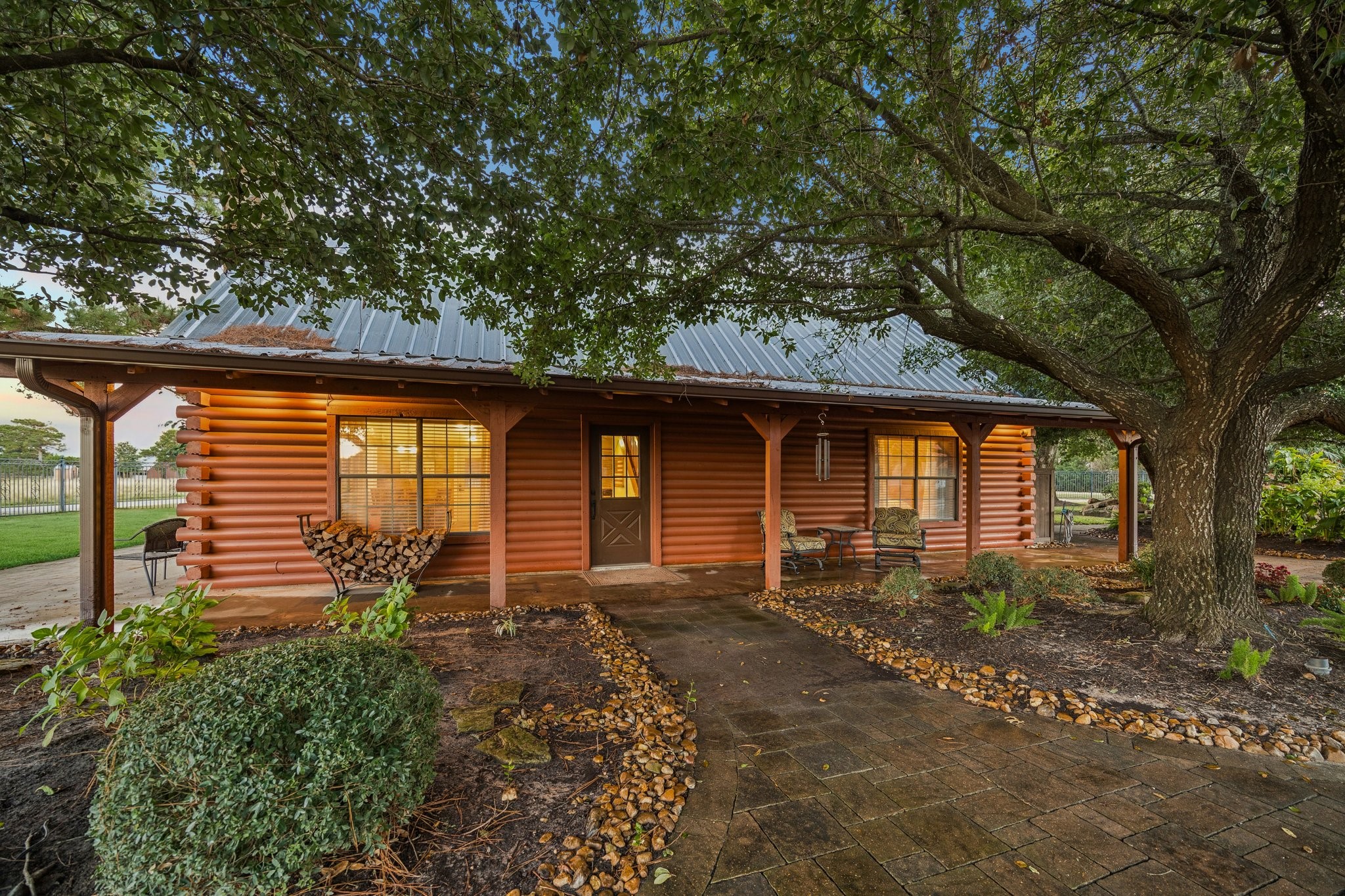 21538 Mueschke Road Tomball, TX 77377 - Photo 8 of 50 Charming log cabin retreat: tucked beneath a canopy of mature trees, this beautifully crafted log cabin exudes warmth, comfort, and rustic elegance. From the moment you arrive, the inviting front porch and stone-lined walkway welcome you to unwind and take in the peaceful surroundings.