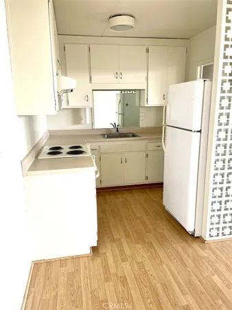 a kitchen with a refrigerator a stove a sink and white cabinets with wooden floor