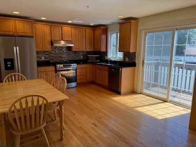 a kitchen with stainless steel appliances kitchen island granite countertop a refrigerator a stove a sink dishwasher and wooden cabinets with wooden floor