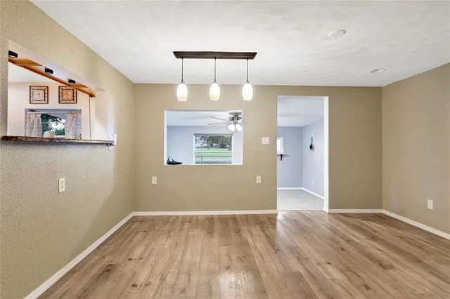 a view of an empty room with wooden floor and a kitchen