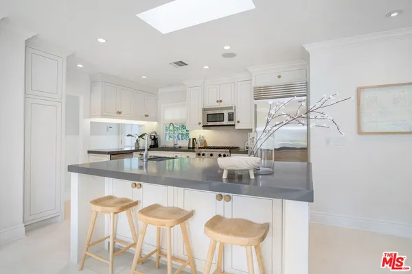 a kitchen with stainless steel appliances granite countertop a sink a stove a refrigerator a microwave and white cabinets with wooden floor