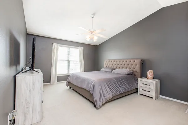 a spacious bedroom with a bed and a flat tv screen on dresser