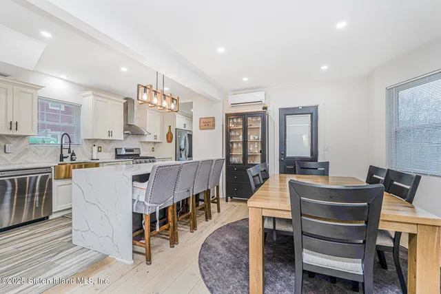 a view of kitchen with stainless steel appliances granite countertop dining table chairs sink and white cabinets