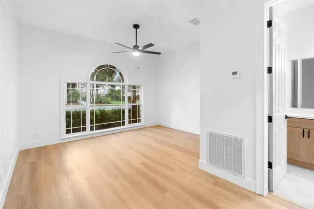 an empty room with wooden floor fan and windows
