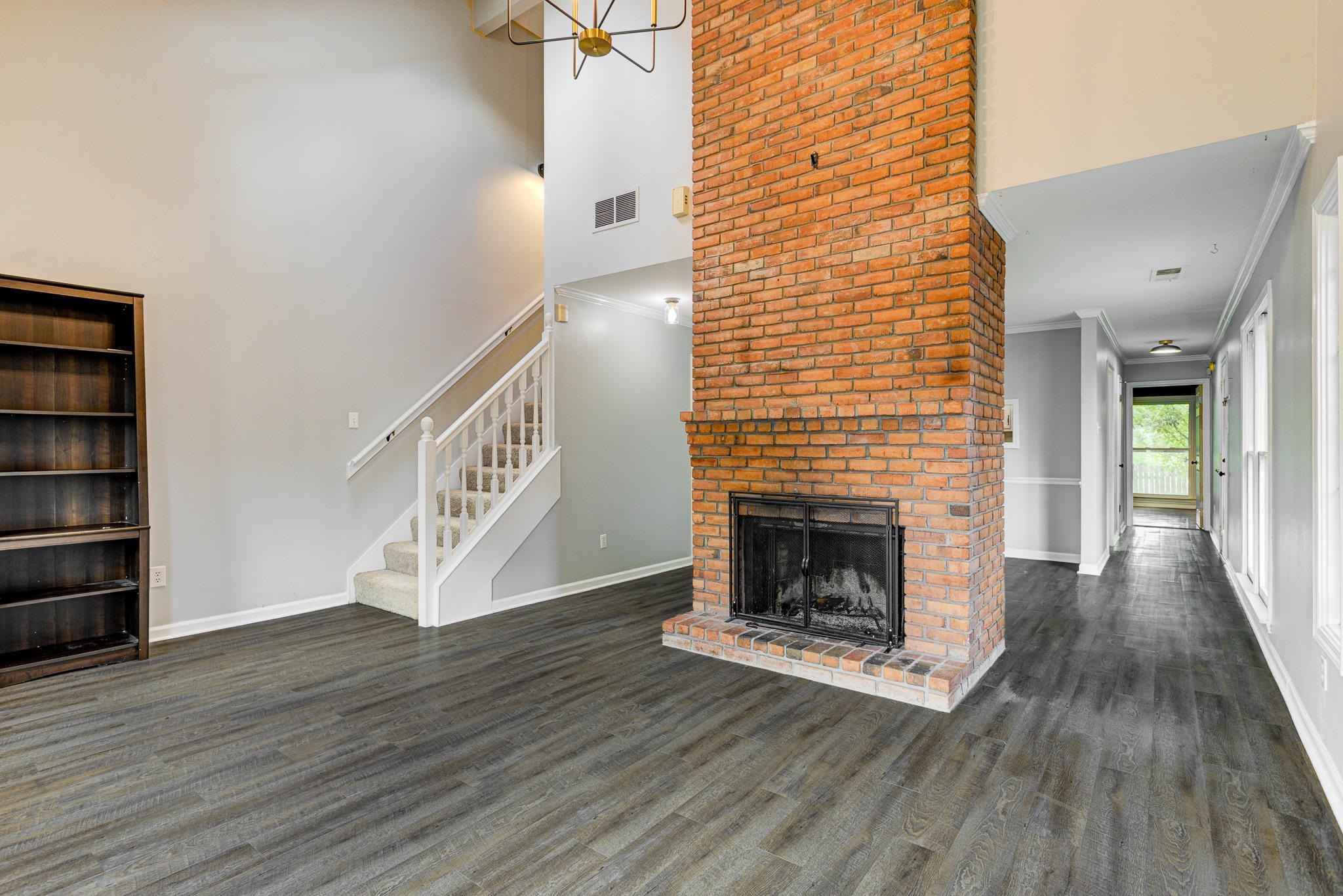 218 South Walnut Bend Road Memphis, TN 38018 - Photo 6 of 25 Unfurnished living room featuring a towering ceiling, dark wood-style floors, stairway, a brick fireplace, and crown molding