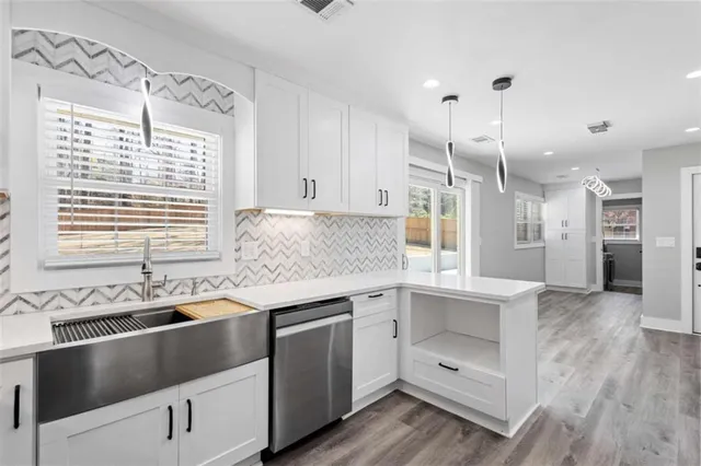 a view of an empty room and kitchen with wooden floor