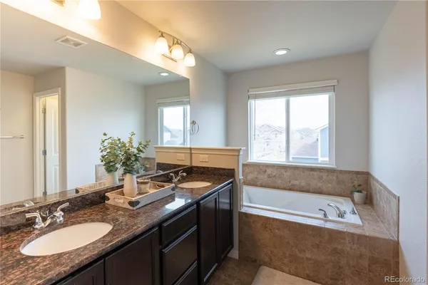 a bathroom with a granite countertop tub a double vanity sink and mirror