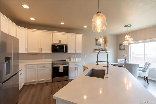 a kitchen with stainless steel appliances granite countertop a sink dishwasher a refrigerator and a dining table with wooden floor