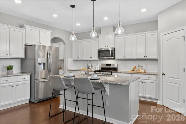 a kitchen with kitchen island granite countertop a refrigerator a stove a sink and white cabinets with wooden floor