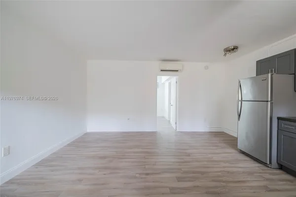 a view of an empty room with wooden floor and a refrigerator