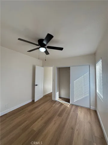 a view of an empty room with wooden floor and a ceiling fan