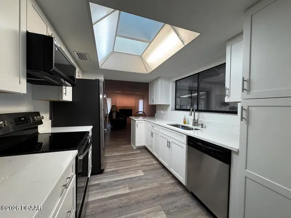 a large kitchen with a large counter top space a sink stainless steel appliances and cabinets