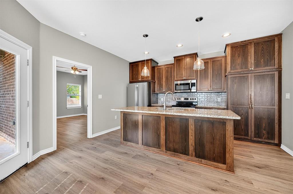 508 Goodjohn Street Collinsville, TX 76233 - Photo 11 of 40 Kitchen with stainless steel appliances, decorative backsplash, light stone countertops, an island with sink, and ceiling fan