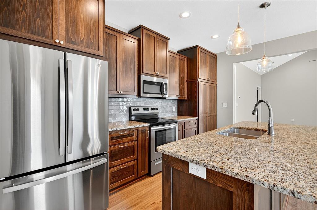 508 Goodjohn Street Collinsville, TX 76233 - Photo 13 of 40 Kitchen featuring appliances with stainless steel finishes, tasteful backsplash, hanging light fixtures, light wood-type flooring, and light stone counters