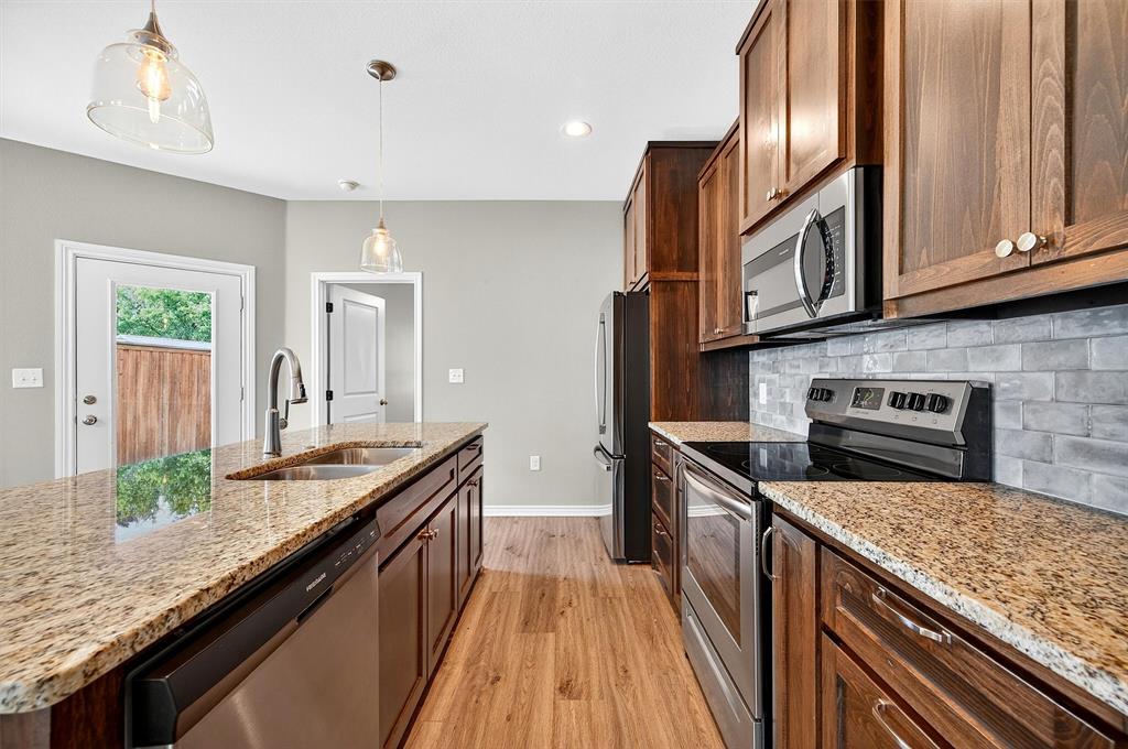 508 Goodjohn Street Collinsville, TX 76233 - Photo 15 of 40 Kitchen featuring appliances with stainless steel finishes, light wood-style floors, pendant lighting, light stone counters, and backsplash