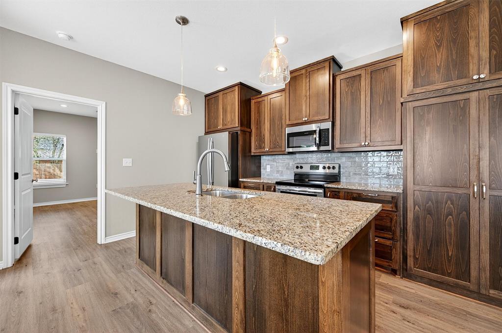 508 Goodjohn Street Collinsville, TX 76233 - Photo 9 of 40 Kitchen with backsplash, light stone counters, stainless steel appliances, decorative light fixtures, and light wood-style floors