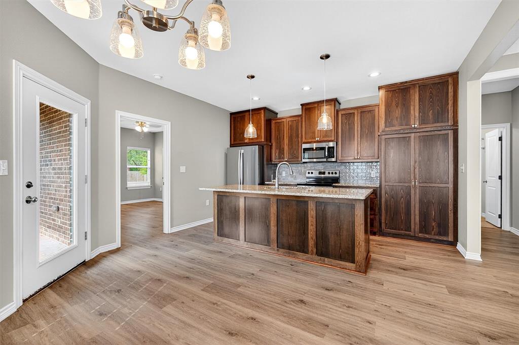 508 Goodjohn Street Collinsville, TX 76233 - Photo 10 of 40 Kitchen with hanging light fixtures, tasteful backsplash, appliances with stainless steel finishes, an island with sink, and light wood-type flooring