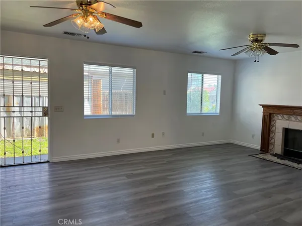 an empty room with wooden floor a chandelier fan and windows