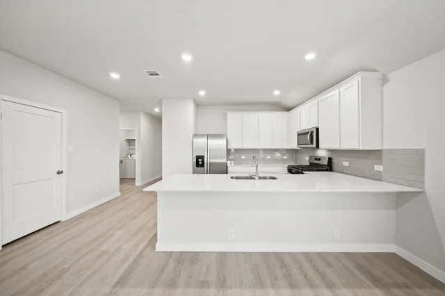 a large white kitchen with kitchen island a sink stainless steel appliances and cabinets