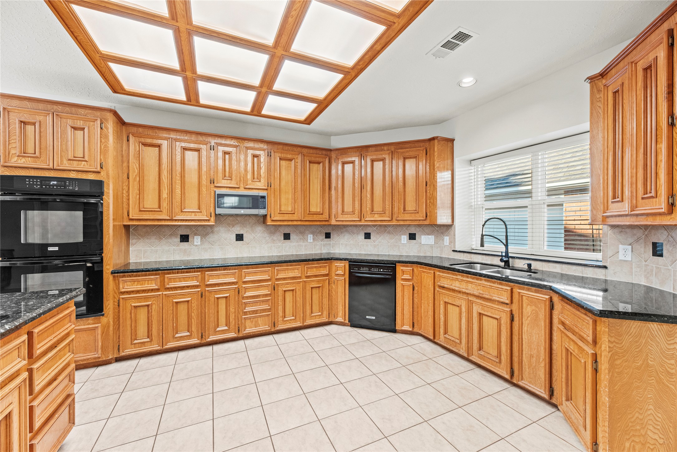 12502 Pavilion Court Tomball, TX 77377 - Photo 11 of 37 Fabulous kitchen with granite counters, tile backsplash with decorative inlay, black appliances, double ovens and a large window above the sink.