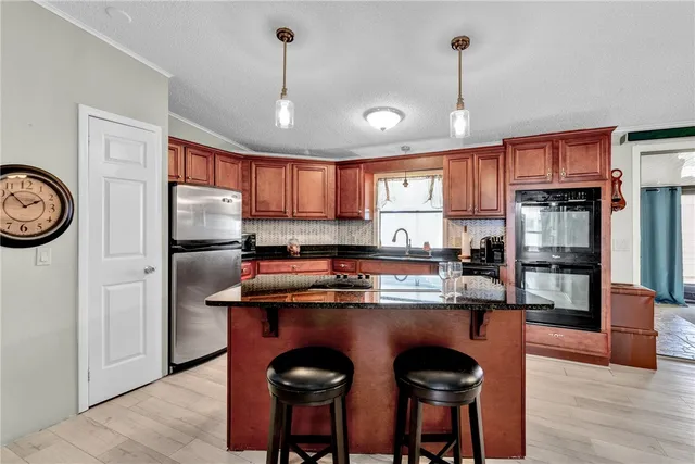 a kitchen with stainless steel appliances granite countertop a refrigerator a sink dishwasher a stove and a dining table with wooden floor