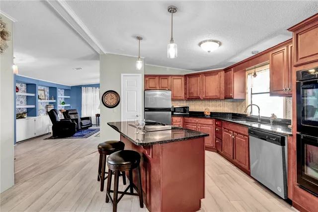 a kitchen with stainless steel appliances kitchen island granite countertop a stove a sink a dining table and chairs with wooden floor