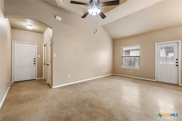 an empty room with chandelier fan and windows