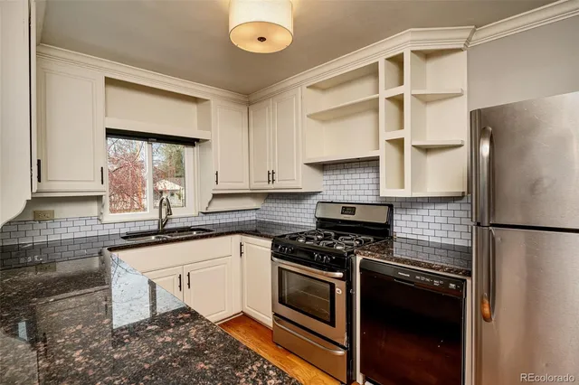 a kitchen with granite countertop a refrigerator a sink and white cabinets