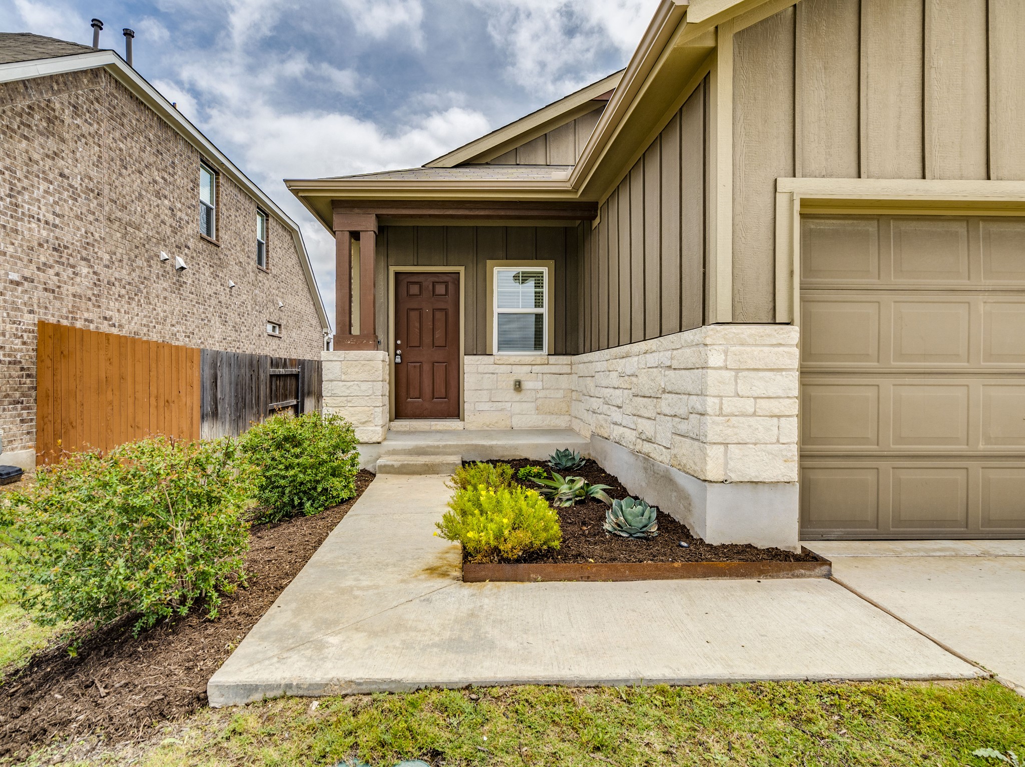 790 Pepperbark Loop Buda, TX 78610 - Photo 3 of 22 A welcoming entry features a rich wooden door, framed by stone accents and meticulously landscaped plantings.