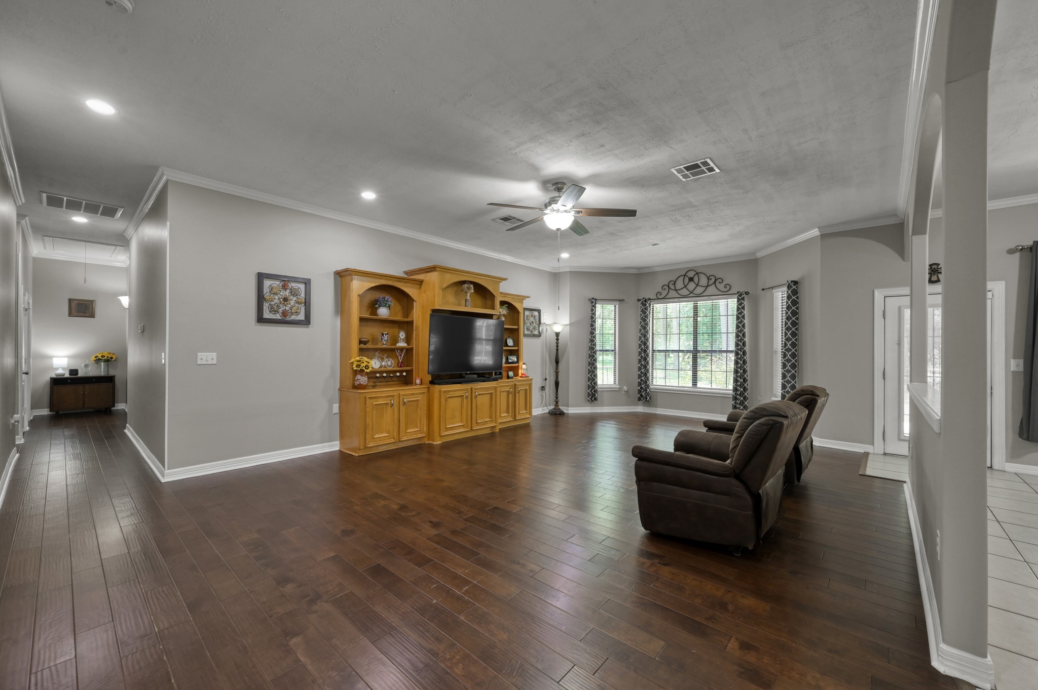 910 Commons Way Court Huffman, TX 77336 - Photo 6 of 49 This spacious living room features dark hardwood floors, a large built-in entertainment center, and ample natural light from multiple windows. The neutral walls and ceiling fan enhance the room's modern comfort, while the open layout connects seamlessly to adjacent spaces.