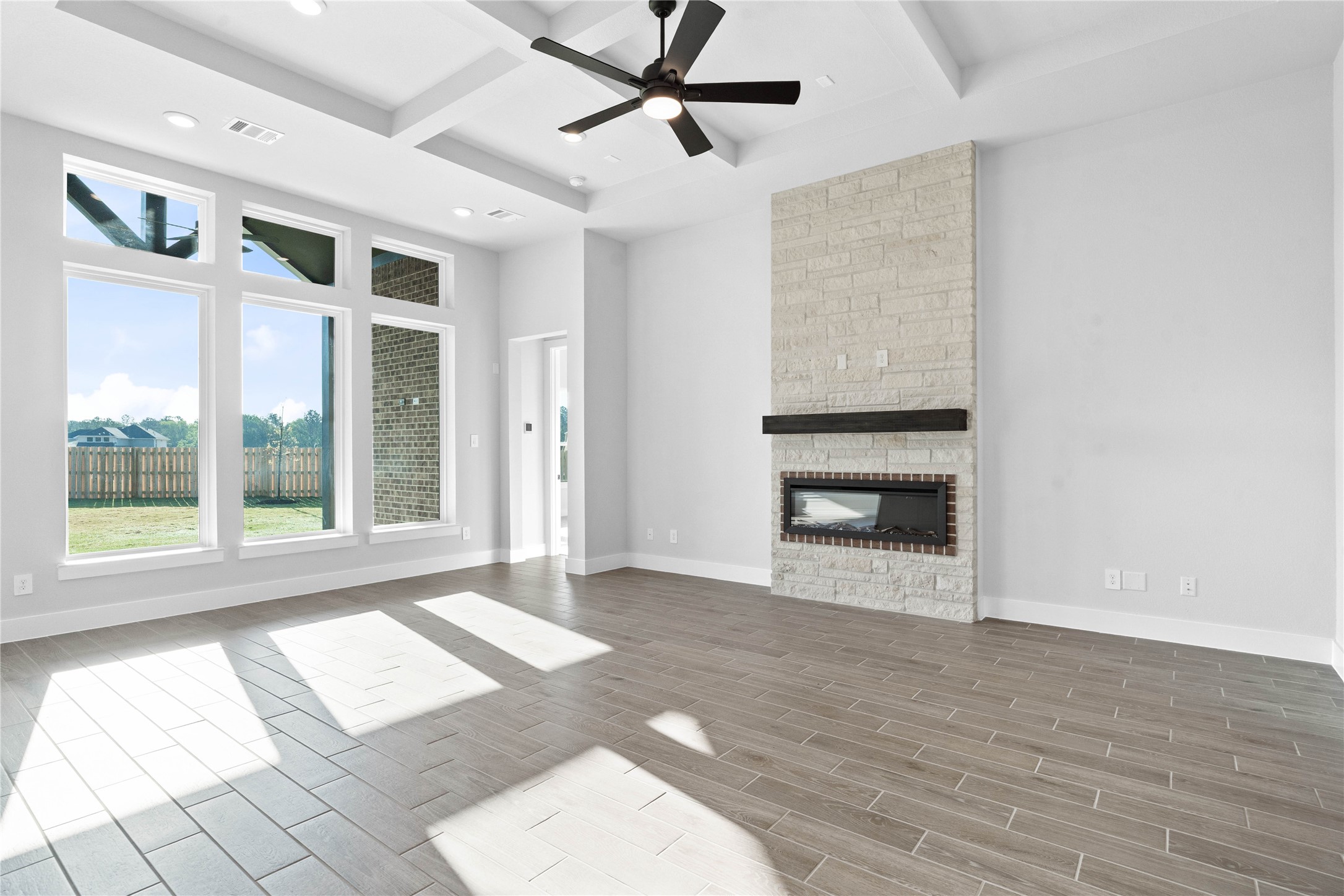 2114 Rowl Street Montgomery, TX 77316 - Photo 19 of 50 A stately floor-to-ceiling stone fireplace serves as the room's focal point, featuring a sleek linear gas insert and a rustic dark-wood mantel. The architectural interest continues overhead with a grand coffered ceiling, accented by integrated LED lighting and a contemporary black ceiling fan.