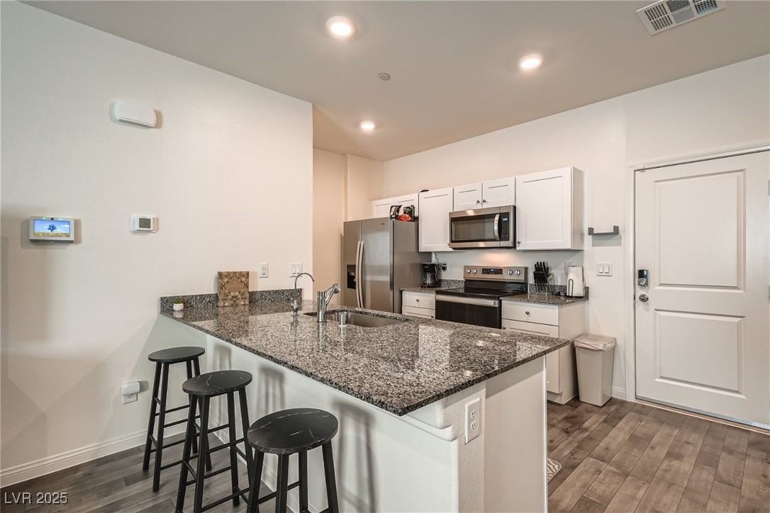 527 Clearsable Avenue Henderson, NV 89044 - Photo 3 of 11 Kitchen featuring a kitchen breakfast bar, white cabinets, dark stone countertops, dark wood-type flooring, and stainless steel appliances