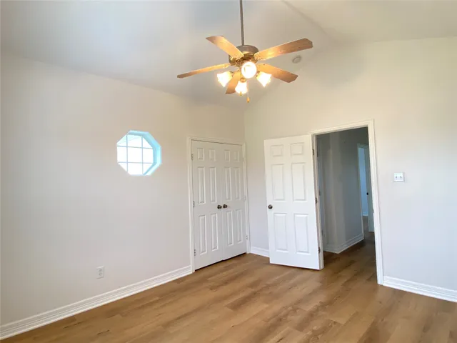 an empty room with wooden floor fan and windows