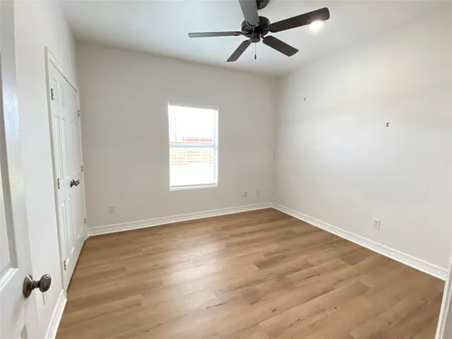 an empty room with wooden floor fan and windows