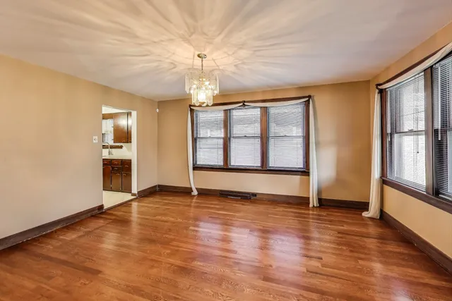 an empty room with wooden floor chandelier and windows