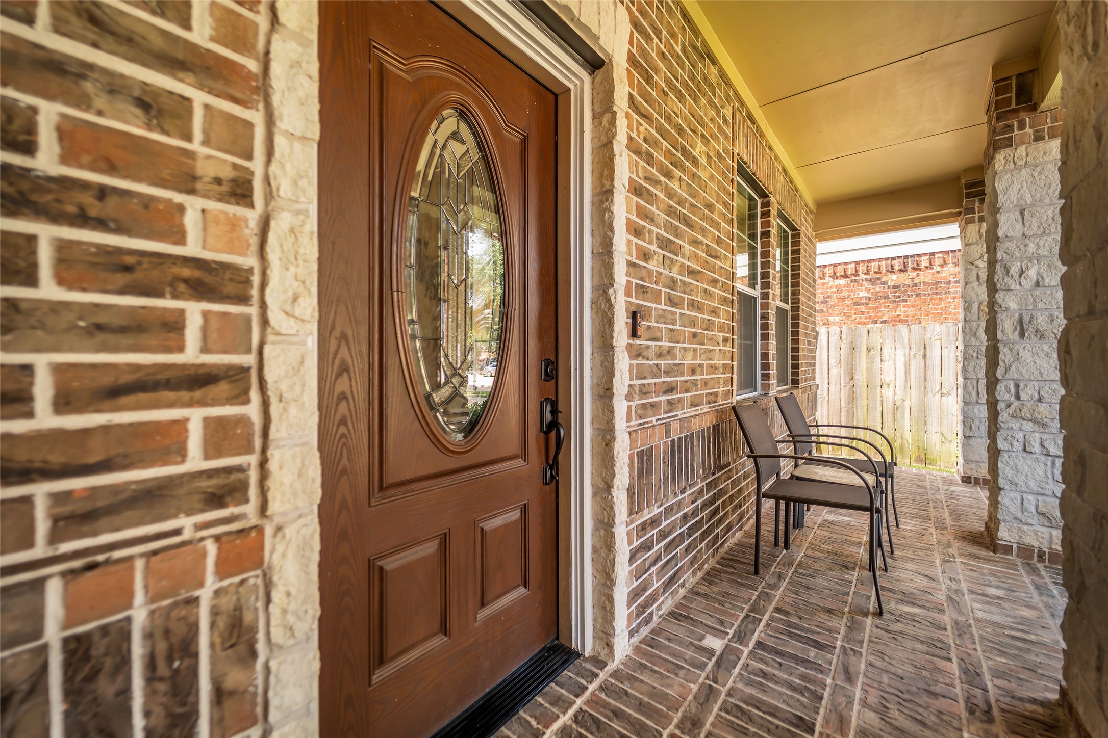 5406 Quarry Ridge Road Richmond, TX 77407 - Photo 4 of 36 Covered front porch with timeless brick and stone accents, a decorative glass-inset front door, and a welcoming sitting area perfect for enjoying a quiet morning or greeting guests.