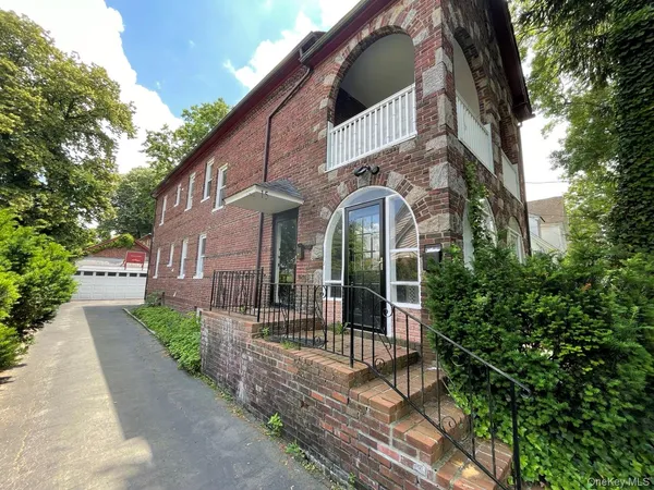 a view of a brick house with a small yard plants and large tree