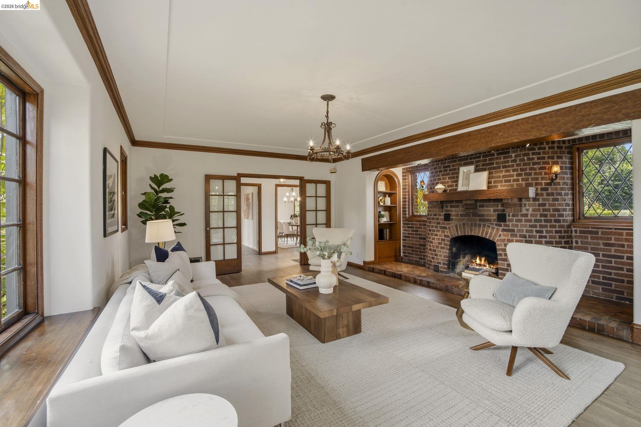 1087 Hubert Road Oakland, CA 94610 - Photo 7 of 67 Living area featuring a brick fireplace with a wood mantle, wood-frame windows, wood-finish flooring, and a decorative chandelier
