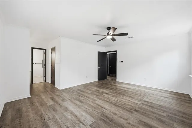 a view of an empty room with wooden floor and a ceiling fan