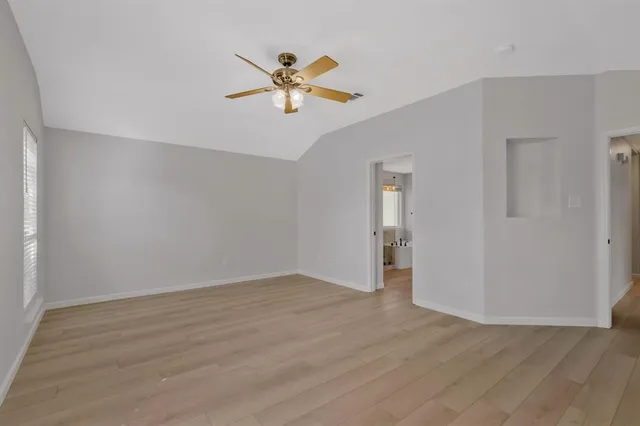 a view of an empty room with wooden floor and a ceiling fan
