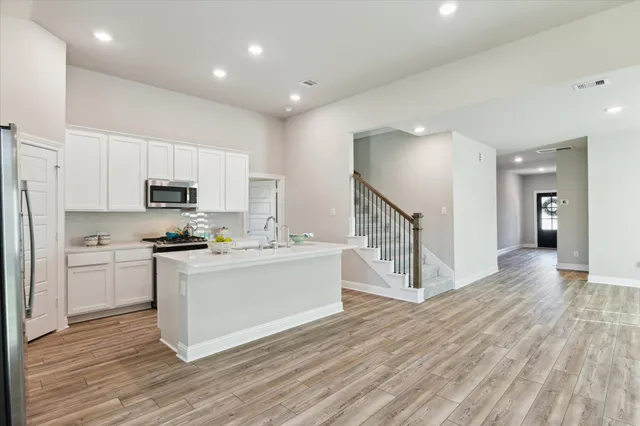 a kitchen with stainless steel appliances granite countertop a stove top oven a sink dishwasher and a refrigerator with wooden floor