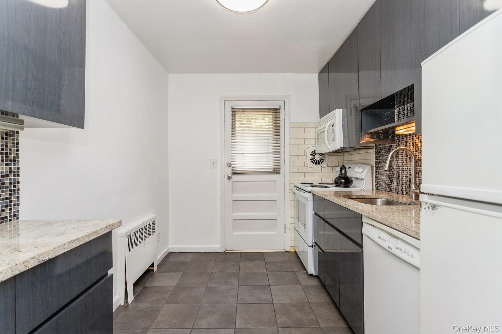 51 Cross Street, Unit 3A Yonkers, NY 10708 - Photo 10 of 17 Kitchen featuring white appliances, tasteful backsplash, radiator, dark tile patterned flooring, and light stone counters