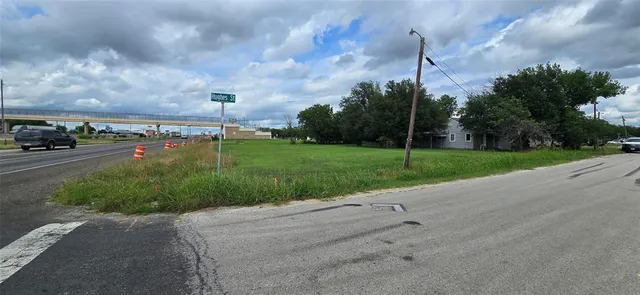 a view of a street with a big yard and a large tree