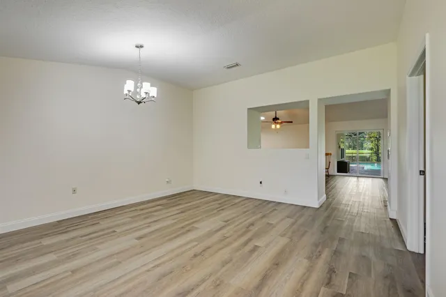 an empty room with wooden floor chandelier and windows