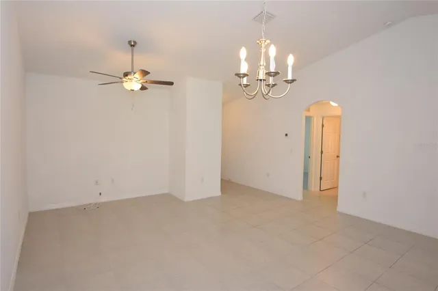 an empty room with a chandelier fan and kitchen view