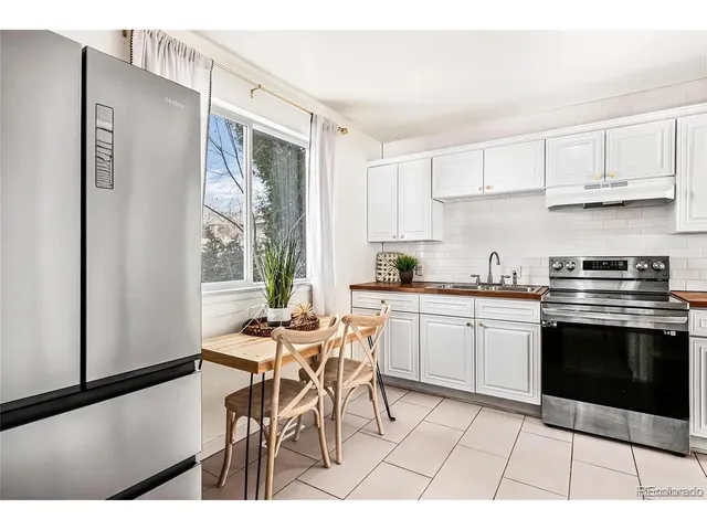 a kitchen with stainless steel appliances kitchen island granite countertop a refrigerator a stove a sink and white cabinets with wooden floor