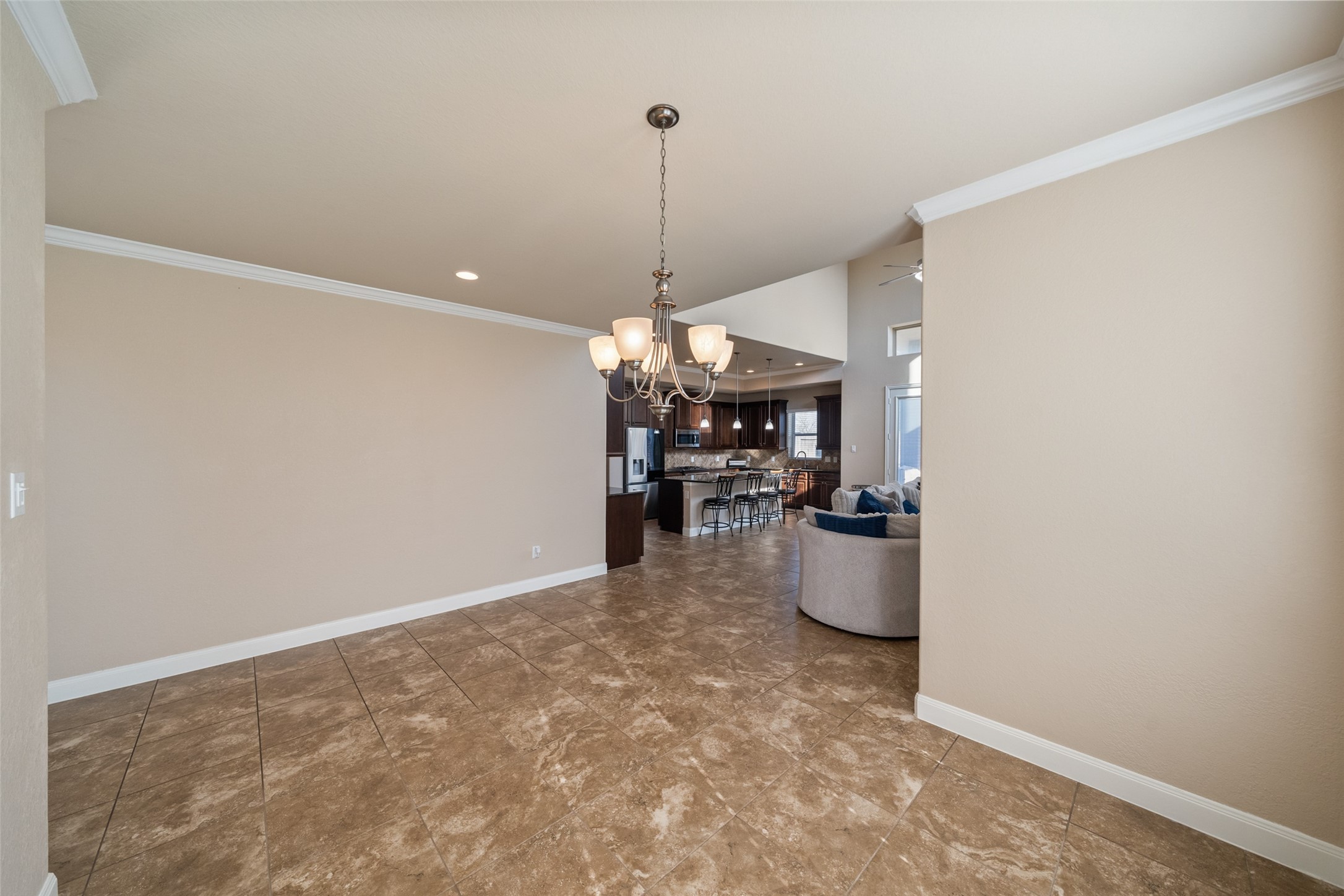 4747 Abercorn Street Rosharon, TX 77583 - Photo 9 of 46 This photo showcases a spacious open-concept area with tile flooring, neutral walls, and a modern chandelier. It leads into a kitchen with a breakfast bar and adjacent living space, creating a welcoming and functional layout.