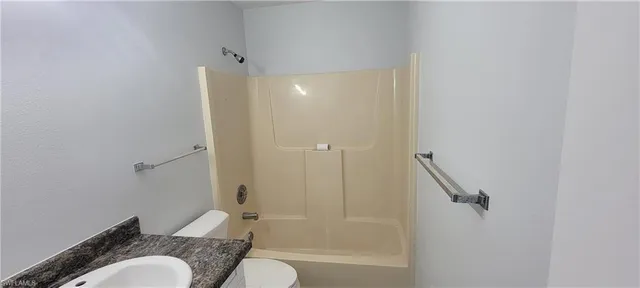 a bathroom with a granite countertop bathtub shower sink vanity and toilet