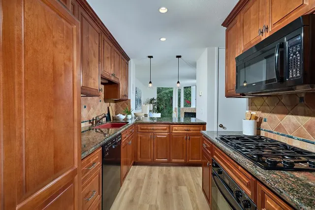 a kitchen with stainless steel appliances granite countertop a stove a sink dishwasher and a refrigerator with wooden cabinets
